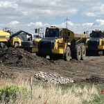 Large dump trucks sit parked at a highway construction site in Alberta.