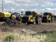 Large dump trucks sit parked at a highway construction site in Alberta.