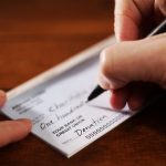 Close-up of a hand holding a pen writing the dollar amount on a cheque.