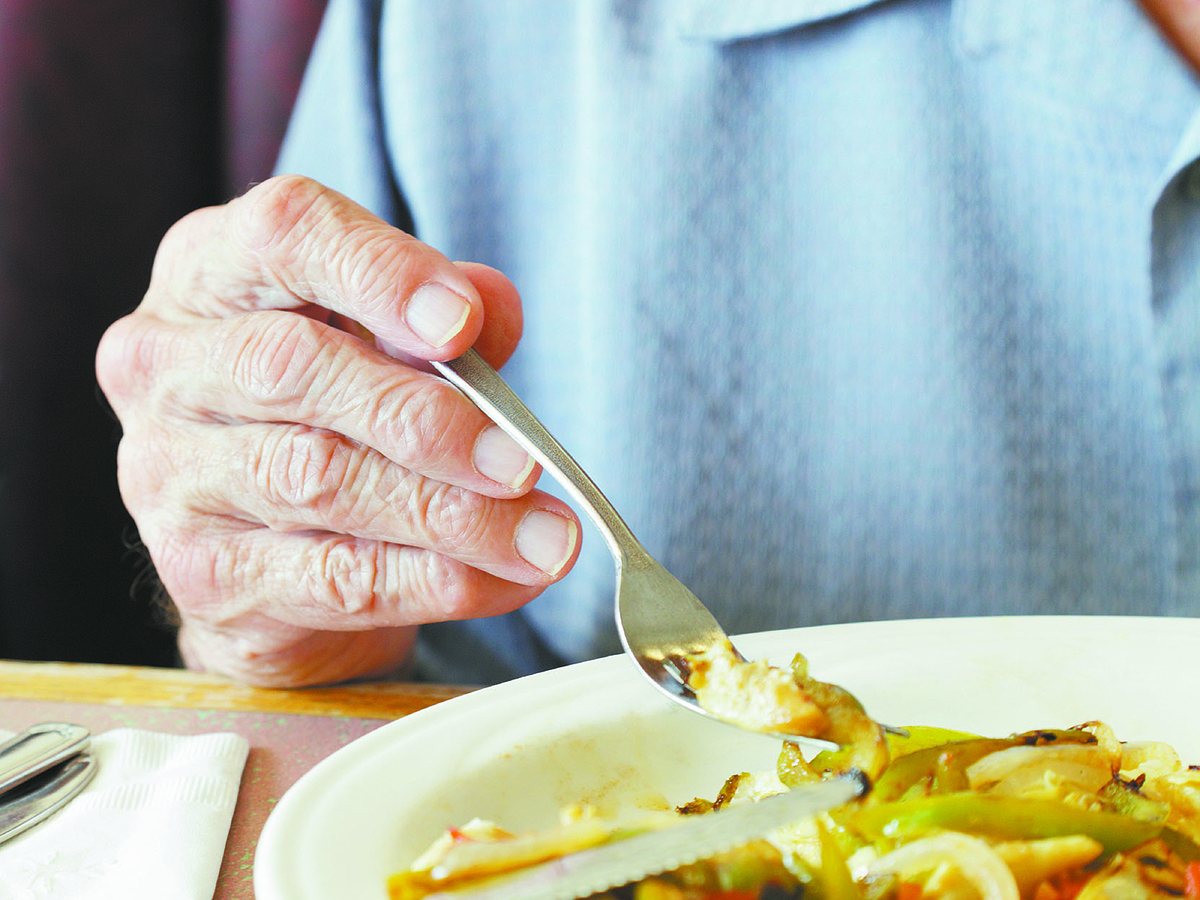 Close-up of the hand of a senior man lifting some food off a plate on a fork.