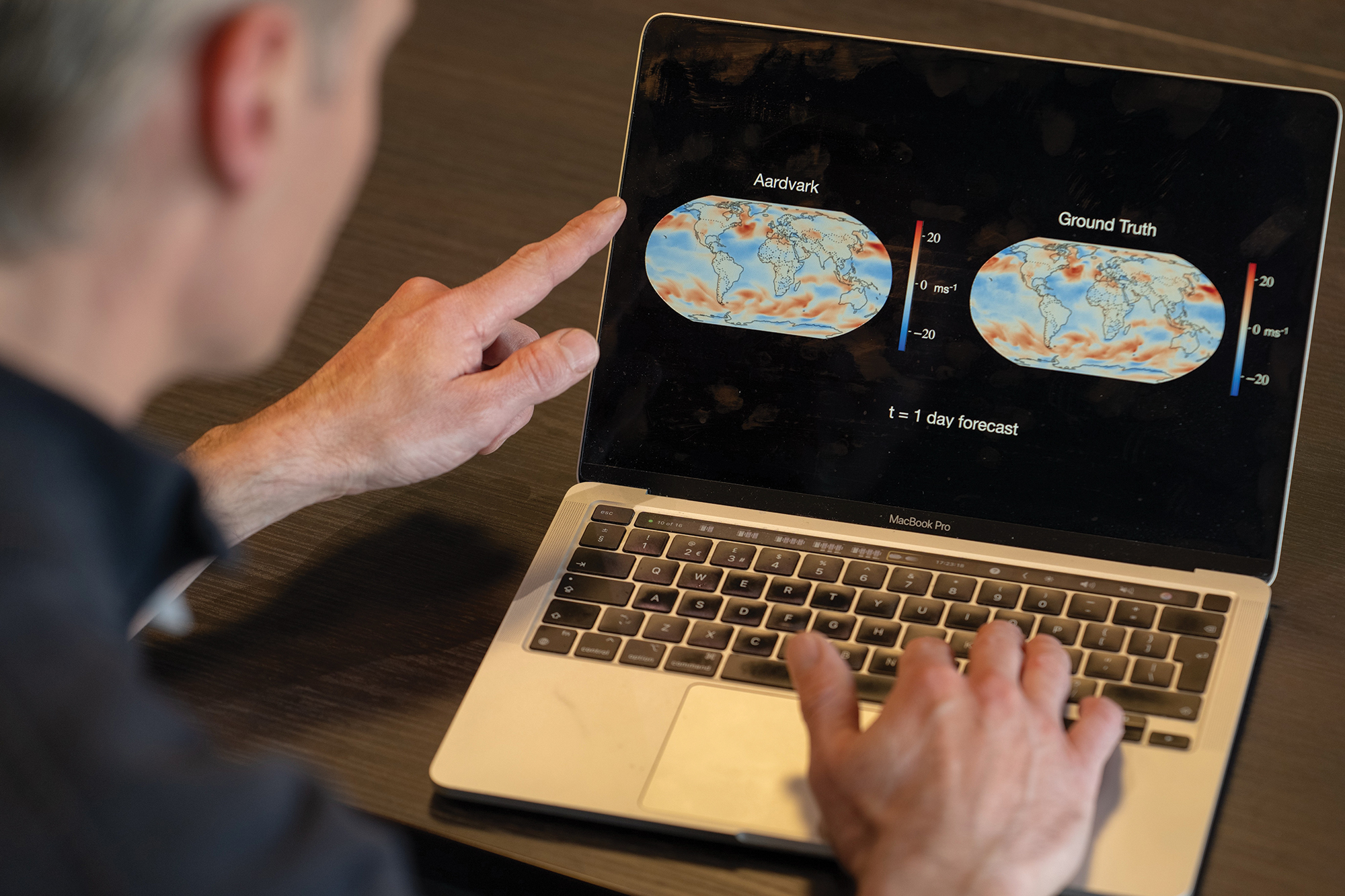 A person points at a laptop screen displaying two world maps with weather data, labeled "Aardvark" and "Ground Truth" for a 1-day forecast.