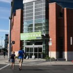 Two people cross a street walkijg towar a building on a corner with a sign on it that reads, "Future Home of Sunterra."
