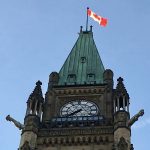 Looking up at a steep angle at the Peace Tower with a Canadian flag on top on Parliament Hill in Ottawa.