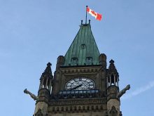 Looking up at a steep angle at the Peace Tower with a Canadian flag on top on Parliament Hill in Ottawa.