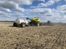An air seeder rig seeds red lentils on a sunny day, with a number of pillowy white clouds in the sky, southeast of Delisle, Saskatchewan.