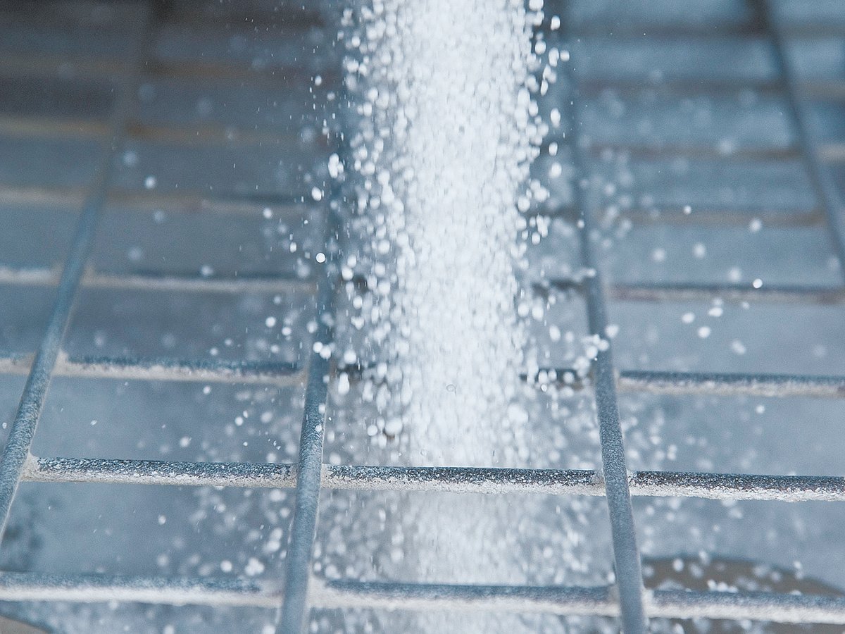 Close-up of the white granules of fertilizer pouring through the grate on an auger's hopper.