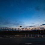 Photo taken from the end of a runway just after sunset as a large passenger jet passes overhead as it is about to land.