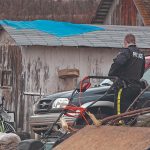 An RCMP officer looks around a cluttered rural yard.