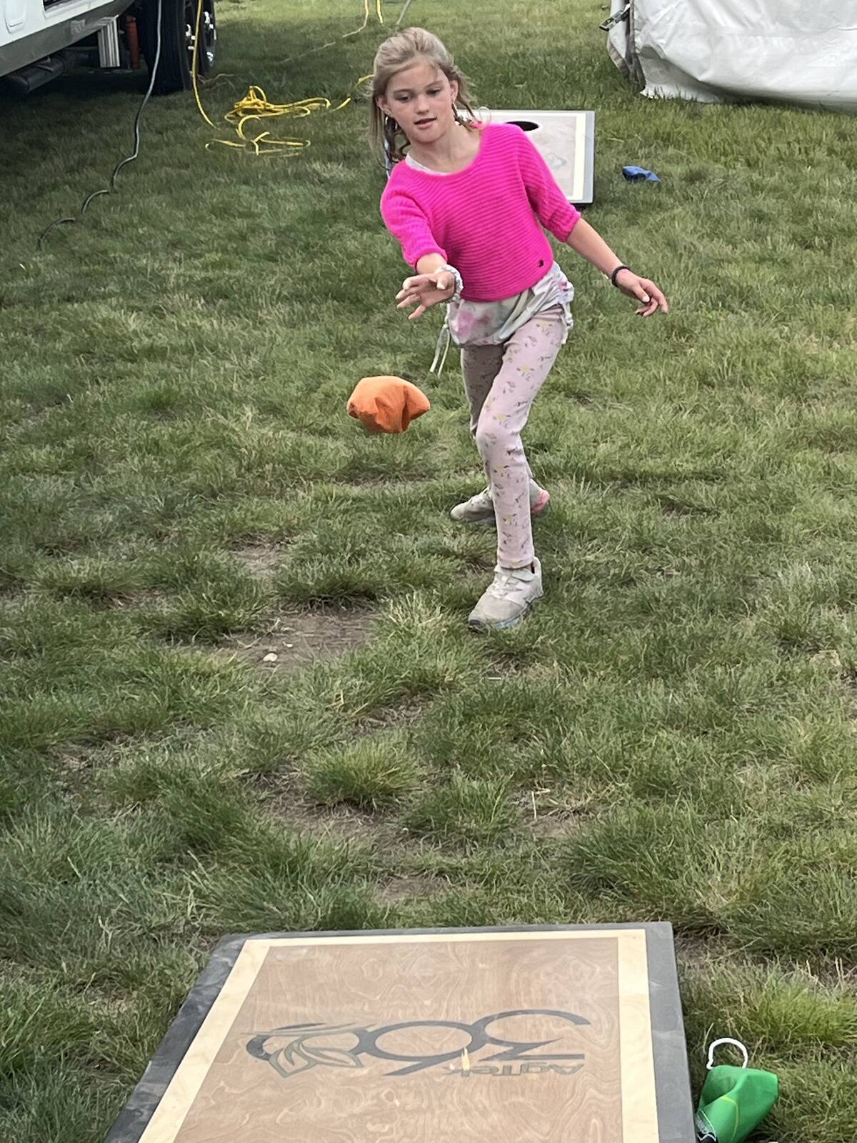 A young girl throws a bean bag toward a corn hole board at Ag in Motion 2025.