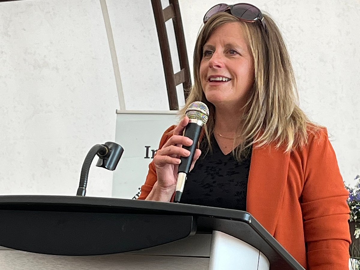 Nichole Neubauer holds a microphone while speaking to a group.