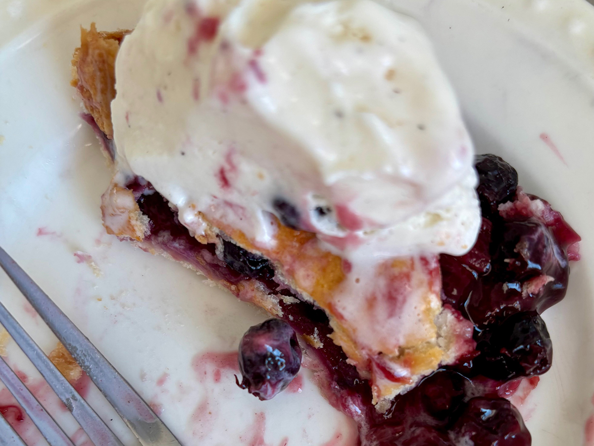 Close-up of a mostly-eaten piece of saskatoon berry pie with vanilla ice cream on top of it.