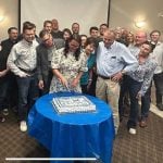 A woman cuts a cake with others standing nearby in a celebration.