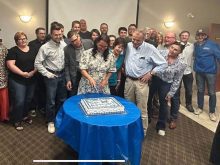 A woman cuts a cake with others standing nearby in a celebration.