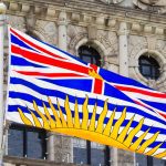 A photo of the flag of British Columbia flying in front of the B.C. legislature in Victoria.