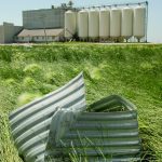 A piece of twisted corrugated metal sits on the grass with an inland grain terminal in the background.