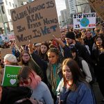 Protesters crowd a street carrying signs that read, "Global warming real. In other news, water is wet," and "Stop denying the [blue painted pic of the Earth] is dying."