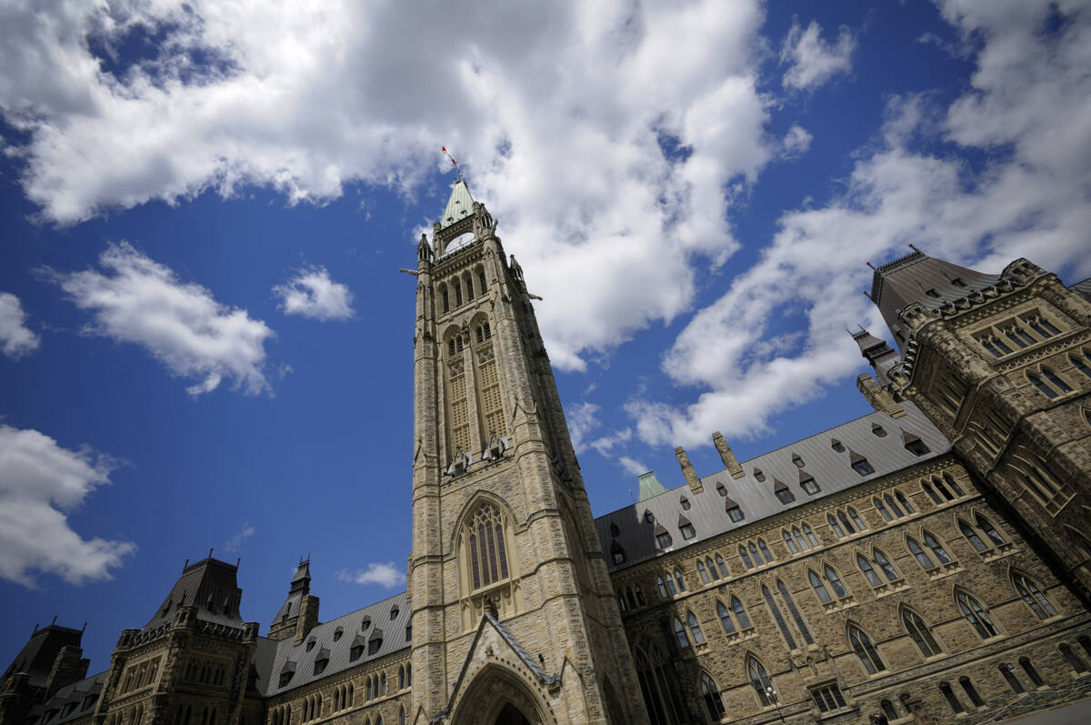 Looking upward at the Peace Tower on Parliament Hill in Ottawa. The sky in the background is brilliant blue with a few puffy white clouds.