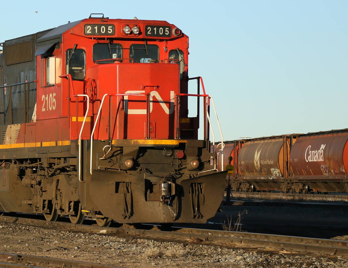 A CN engine sits on the tracks in a rail yard with grain cars visible in the background.