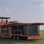 PhiBer Manufacturing's Dash drone tender trailer sits attached to a truck at the drone flying area at the Ag in Motion farm show near Langham, Sask., while operators sit atop the trailer flying a large drone visible in the distance.
