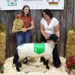Two women pose with the "Supreme Champion Ram" at a sheep show.
