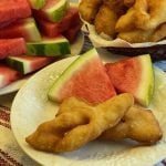 A photo of some Mennonite fried bread called "Roll Kuchen" on a plate with a couple triangles of sliced watermelon.