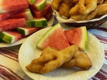 A photo of some Mennonite fried bread called "Roll Kuchen" on a plate with a couple triangles of sliced watermelon.