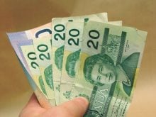 A man's hand holds at least five Canadian $20 bills and two or three $10 bills in the shape of a fan.