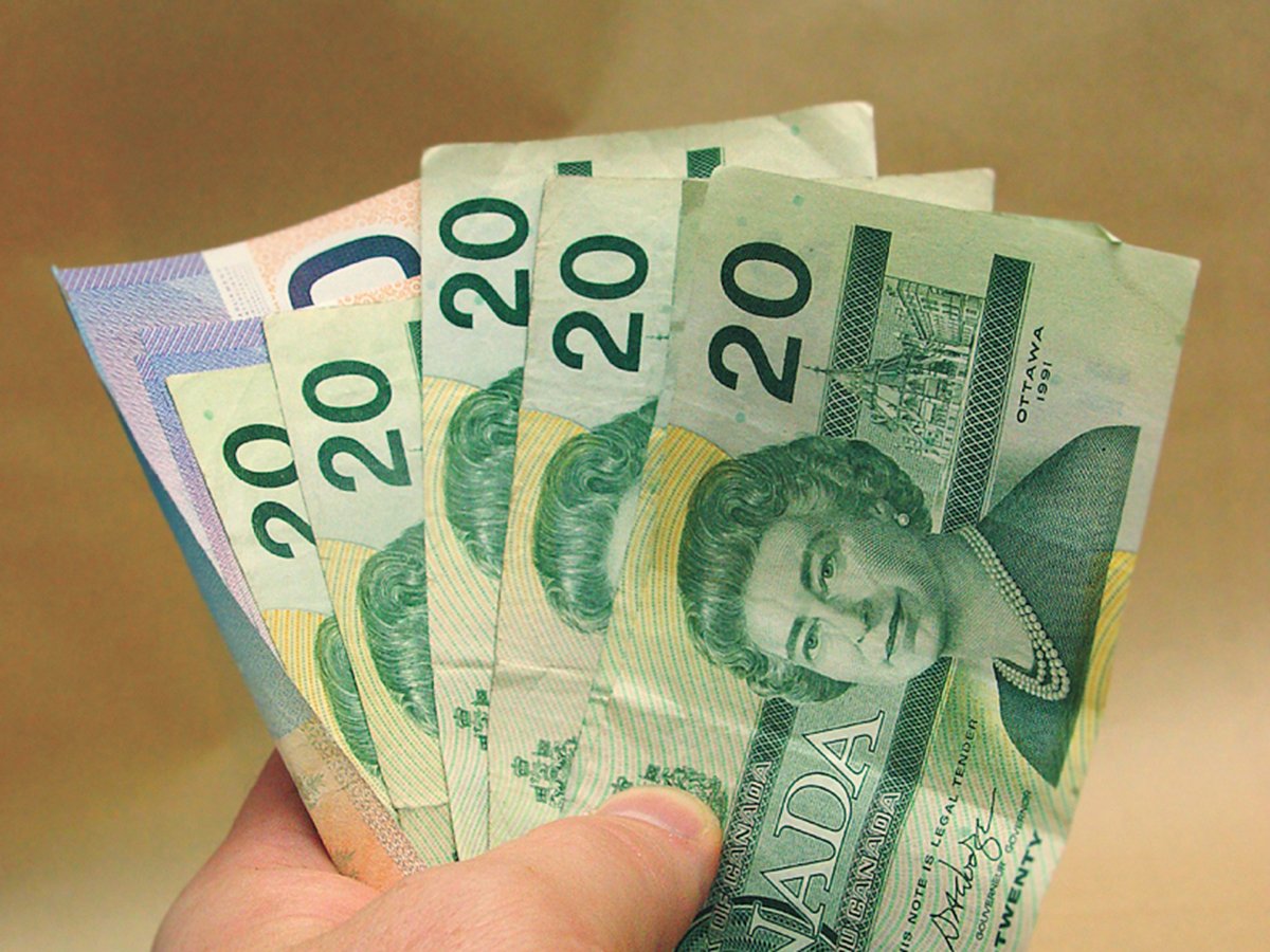 A man's hand holds at least five Canadian $20 bills and two or three $10 bills in the shape of a fan.