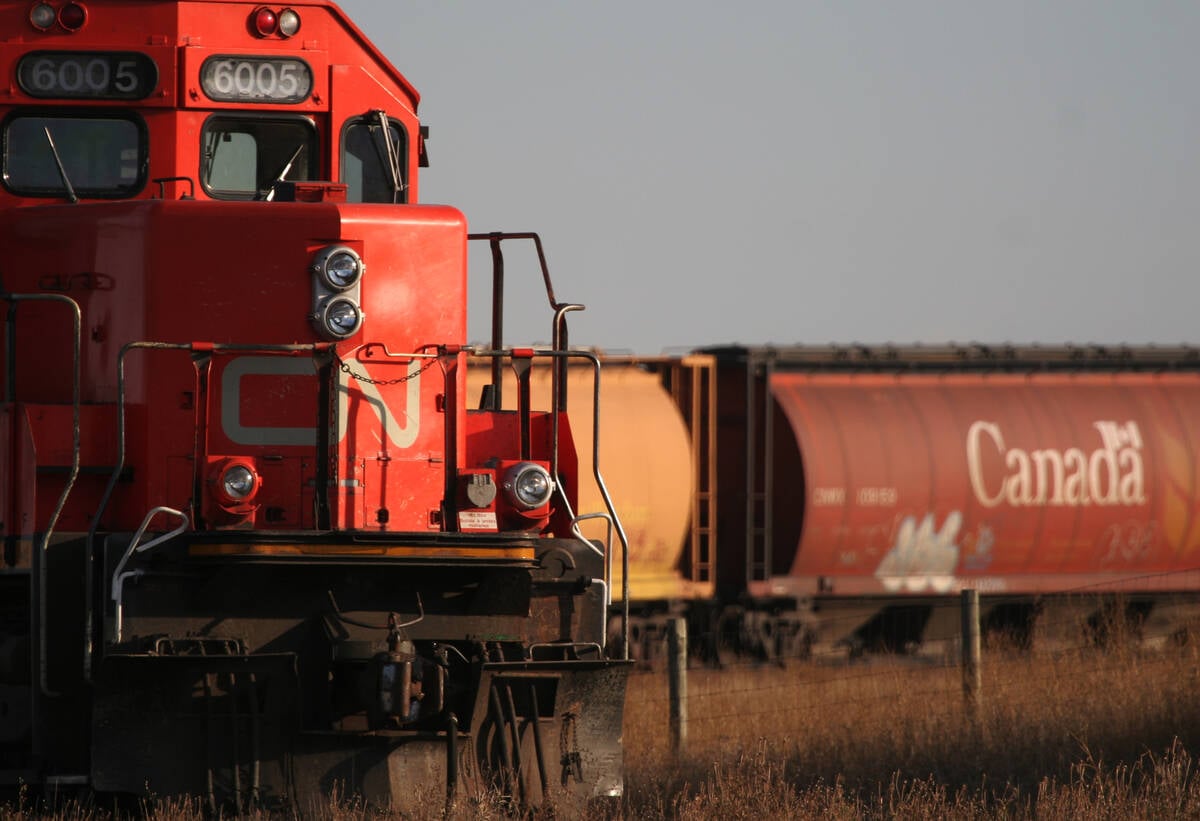 The nose of a CN train engine rounding a corner is in the foreground with its grain cars visible in the background.