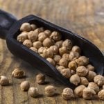 A black scoop holds chickpeas on a wooden tabletop.