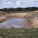 A photo of th low water level in a dugout on a summer day with scattered clouds.