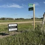 A realtor's "For Sale" sign sits on a corner in rural Saskatchewan next to signpost with signs for "RGE. RD. 3080" and "TWP. RD. 343" on it.