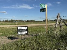 A realtor's "For Sale" sign sits on a corner in rural Saskatchewan next to signpost with signs for "RGE. RD. 3080" and "TWP. RD. 343" on it.