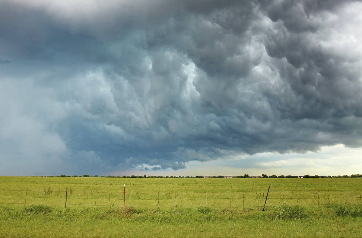 Dark storm clouds over a pasture with a page wire fence in the foreground.