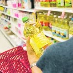 A shopper holds a clear plastic container of golden vegetable oil in her hand and looks at it in the aisle of a grocery store.