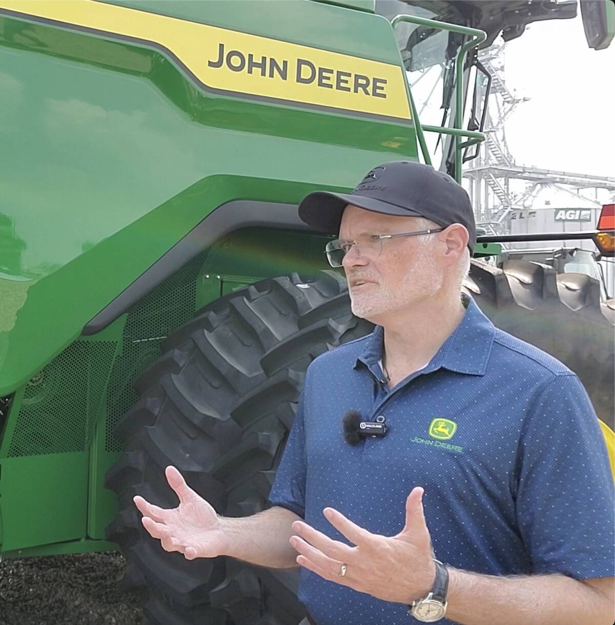 Aaron Wetzel, John Deere vice-president, stands beside one of his company's combines talking and gesturing with his hands at the Ag in Motion farm show near Langham, Saskatchewan in July, 2025.
