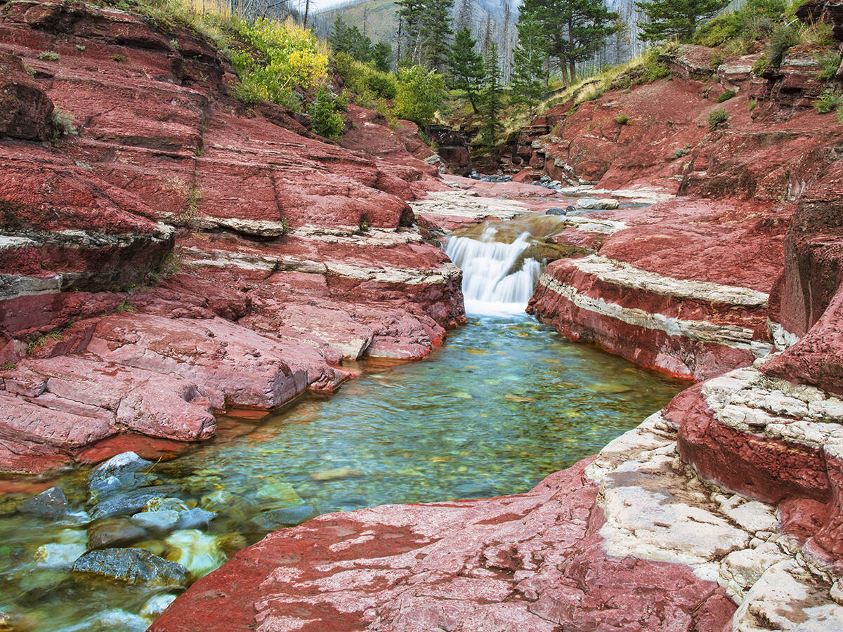 A small waterfall flows over red rock in Red Rock Canyon, Waterton Lakes National Park.