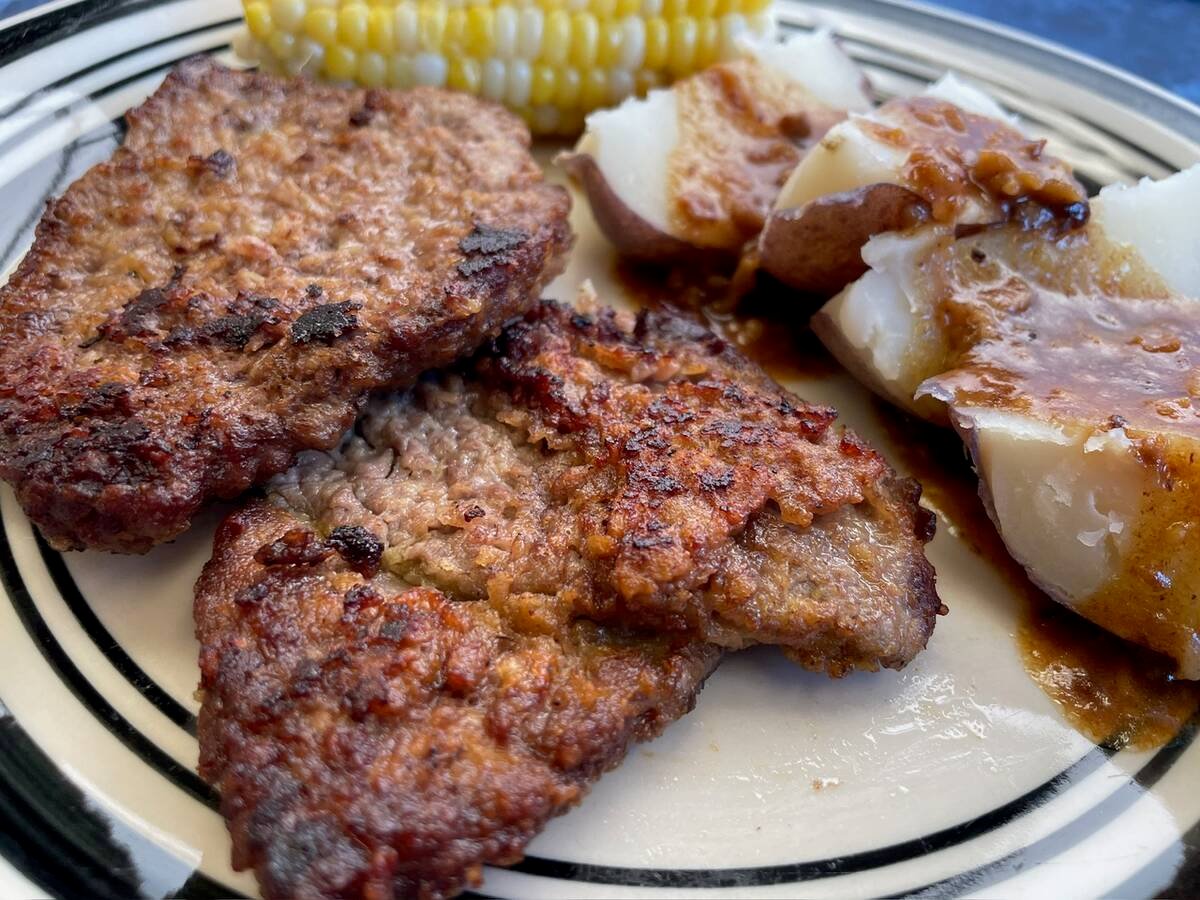 Two pieces of ranch steak, a cob or corn and some quartered potatoes, with skin still on and some pan gravy poured overtop, sit on a plate.