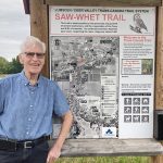 Sinclair Harrison stands on the Trans Canada Trail, next to a trail map built into a log frame, at Lumsden, Saskatchewan, in the fall of 2024.