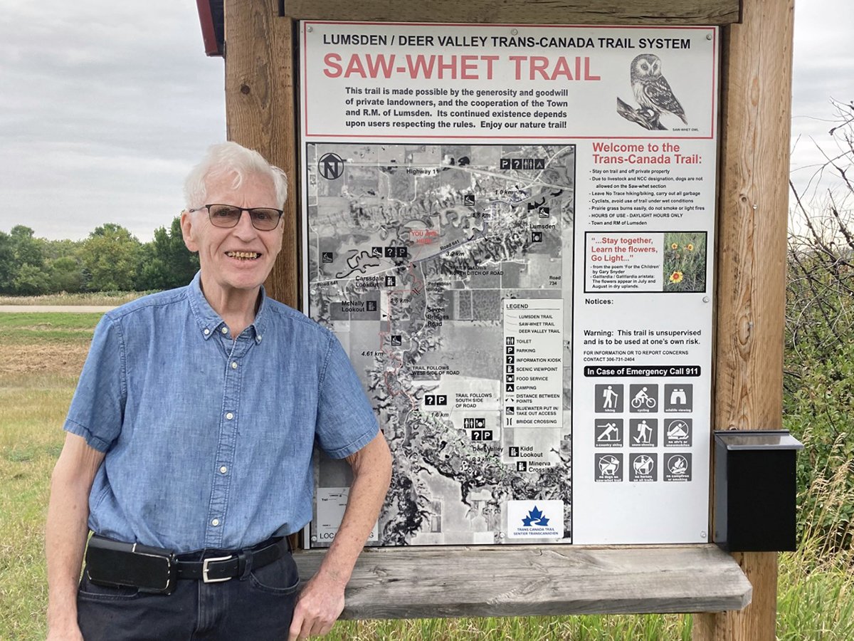 Sinclair Harrison stands on the Trans Canada Trail, next to a trail map built into a log frame, at Lumsden, Saskatchewan, in the fall of 2024.