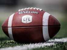 Close-up of a Wilson CFL leather football sitting on the green turf with a white painted stripe beneath the football on the turf.
