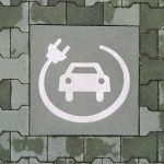 A painted symbol on a green pavement indicates a reserved parking space for electric vehicle charging. The white icon features a car with a charging cable and plug, emphasizing the transition to sustainable mobility and eco-friendly transportation.