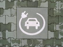 A painted symbol on a green pavement indicates a reserved parking space for electric vehicle charging. The white icon features a car with a charging cable and plug, emphasizing the transition to sustainable mobility and eco-friendly transportation.