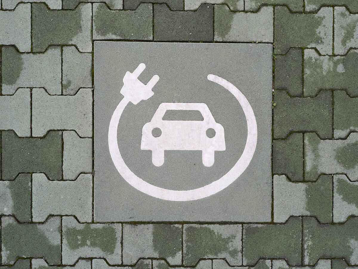 A painted symbol on a green pavement indicates a reserved parking space for electric vehicle charging. The white icon features a car with a charging cable and plug, emphasizing the transition to sustainable mobility and eco-friendly transportation.