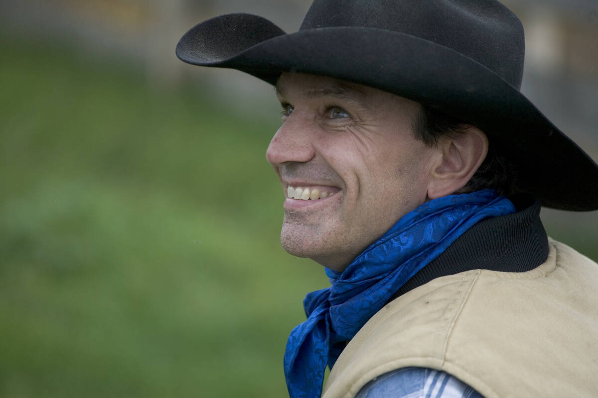 A cowboy in a black hat, Reg Steward, looks over his left shoulder, smiling.