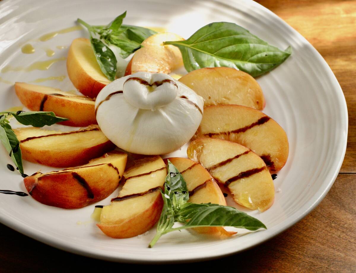 Peaches drizzled with balsamic glaze on a plate with a ball of burrata cheese in the centre and leaves of fresh basil for garnish.