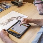 A farmer is seen using a smart device to review data and plan his customized seed application for the day.