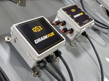 Close-up of a two gray boxes mounted on the sloped roof of a metal grain bin with "GSI GrainVue" written on them, each with multiple black cables entering and exiting.