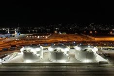 An aerial image of the DP World canola oil transloading facility taken at night, with three large storage tanks all lit up in the foreground.