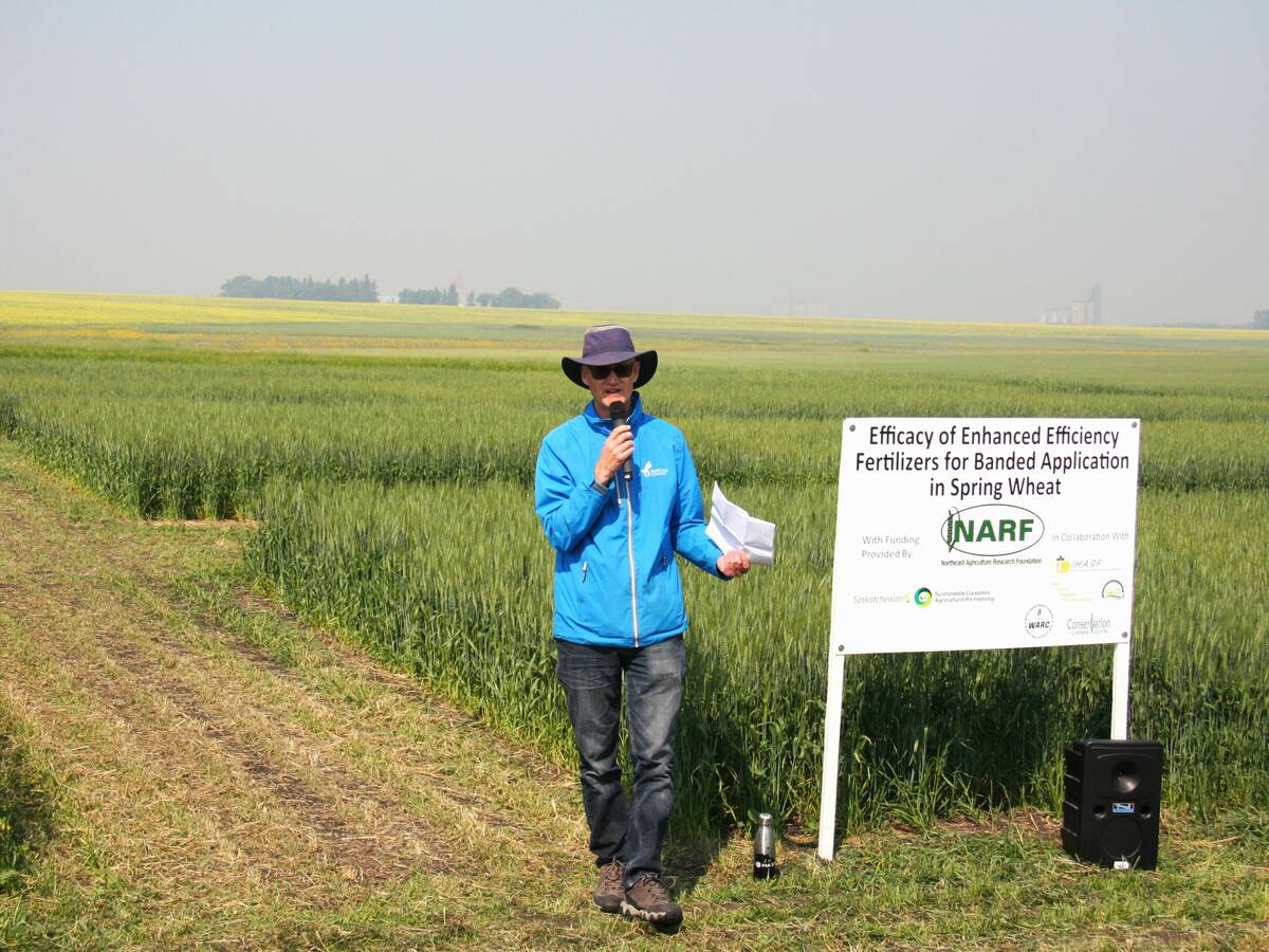 A man in a Tilley hat stands in front of a research plot next to a sign that reads,